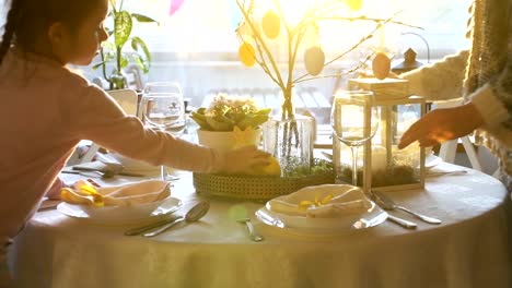 Woman-and-her-little-daughter-are-setting-easter-festive-table-with-bunny-and-eggs-decoration