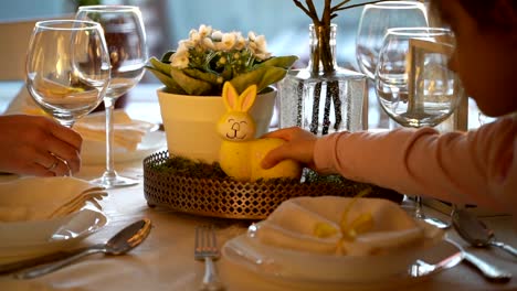 Mujer-y-su-hijita-están-estableciendo-mesa-festiva-de-Pascua-con-conejito-y-huevos-la-decoración