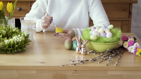 Frau-malt-ein-gelbes-Ei-auf-dem-Tisch-mit-Osterschmuck