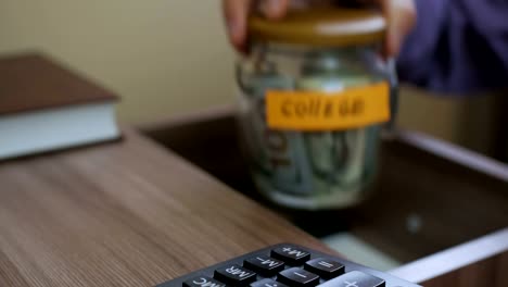 Caucasian-male-putting-a-glass-jar-put-in-a-drawer--table-with-his-savings-for-future-college