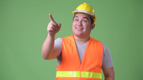 Young-handsome-overweight-Asian-man-construction-worker-against-green-background