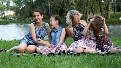 Same-sex-family:-two-mothers-with-two-daughters-play,-laugh-and-have-fun-sitting-in-the-Park-on-the-lawn-at-sunset-near-the-river.