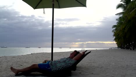 Man-ruht-auf-einer-Sonnenliege-am-Strand-bei-Sonnenuntergang