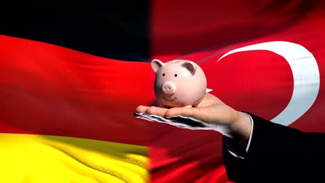 Germany-investment-in-Turkey,-hand-putting-money-in-piggybank-on-flag-background