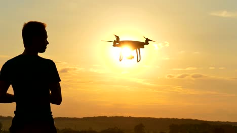 Der-Mann-mit-einem-Quadrocopter-auf-dem-Sonnenuntergang-Hintergrund-spielen