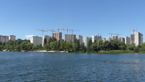 Un-lago-contra-el-fondo-de-las-casas-en-construcción.-Se-construyen-rascacielos-cerca-del-lago.-Construcción-de-edificios-residenciales-cerca-del-lago.