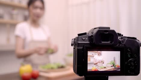 Blogger-Asiatin-mit-Kamera-Aufnahme-wie-gesundes-Essen-Salat-video-für-ihre-Abonnenten,-weibliche-Verwendung-Bio-Gemüse-Salat-vorbereiten-fitten-Körper-zu-Hause-zu-machen.-Gesunde-Ernährung-Konzept.