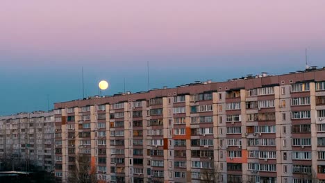 Großer-Vollmond-über-dem-Dach-eines-mehrstöckigen-Gebäudes-bewegt-sich-nach-oben