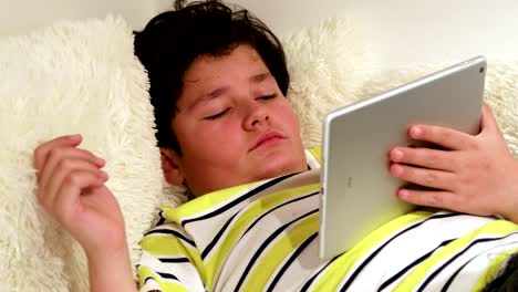 Tired-teen-lying-on-sofa-with-digital-tablet-at-home