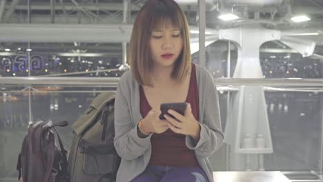 Asiatische-Frau-mit-Smartphone,-während-sie-auf-dem-internationalen-Flughafen-sitzt.