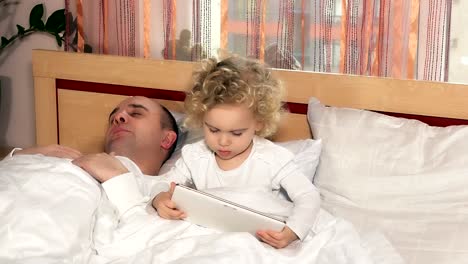 bald-dad-fall-asleep-while-daughter-girl-play-with-tablet-computer-sit-in-bed