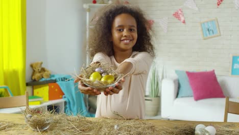 Pequeña-chica-africana-sonriendo-y-posando-con-huevos-de-Pascua-en-hay-nido