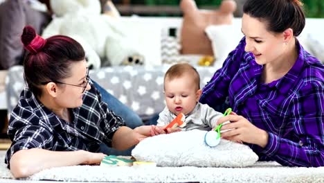 Happy-same-sex-parents-playing-with-little-cute-baby-lying-on-floor-at-home-medium-shot