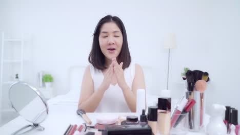 Beauty-Blogger-präsentieren-Beauty-Kosmetik-sitzen-vor-der-Kamera-für-die-Aufnahme-von-Video.-Glücklich-schöne-junge-asiatische-Frau-verwenden-Kosmetik-Rezension-Make-up-Tutorial-übertragen-Live-Video-an-soziale-Netzwerk.