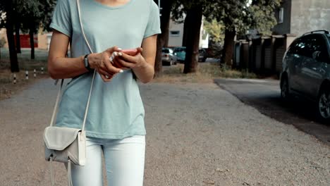 Slim-chica-en-jeans-y-una-camiseta-toma-el-teléfono-de-su-bolso-y-responder-a-un-mensaje-al-aire-libre