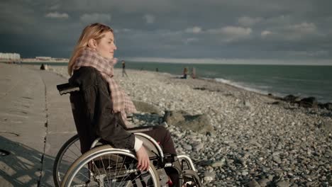 Junge-blonde-Frau-mit-Lähmung-der-Beine-sitzt-im-Rollstuhl,-Blick-auf-Meer