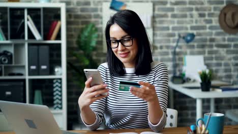 Jovencita-pagando-en-línea-con-tarjeta-de-crédito-usando-teléfono-inteligente-en-el-lugar-de-trabajo