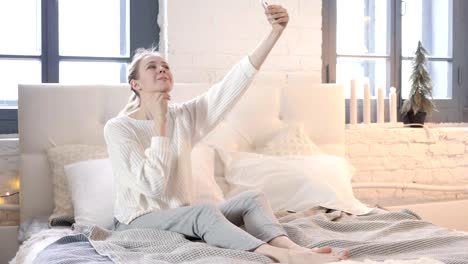 Glückliche-Frau-sitzt-im-Bett-und-macht-Selfie-mit-Handy,-Foto