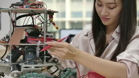 Asian-female-electronics-engineer-works-with-robot,-building,-fixing-robotics-in-workshop.-People-with-technology-or-innovation-concept.