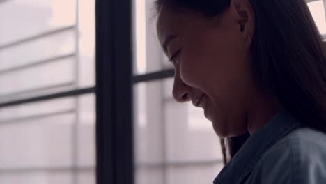 Portrait-young-asian-business-woman-holding-typing-mobile-phone-and-scrolls-through-social-media-feed-in-smartphone-standing-beside-window-at-home-office.