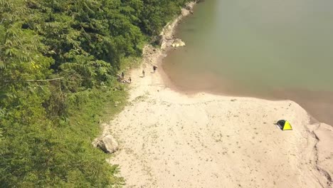 Aerial-view-tourist-people-on-camping-at-river-shore-while-summer-vacation.-Tourist-tent-on-campsite-on-lake-shore-while-summer-hike.-Tourism-and-travel-concept