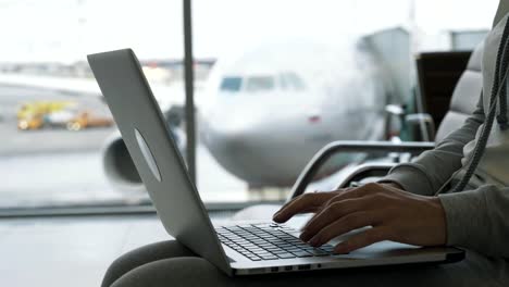 Nahaufnahme-Hände-der-Frau-arbeiten-auf-Laptop-in-Flughafenhalle-Hintergrund-des-Flugzeugs-im-Fenster-wartet-auf-Boarding