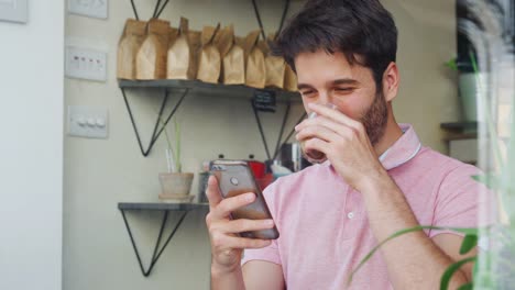 Junger-Mann-in-Coffee-Shop-Blick-auf-Handy