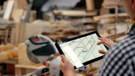 Close-up-of-woodworker-using-tablet-at-work-looking-at-furniture-design