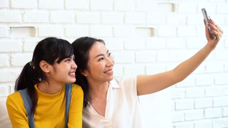 Happy-Asian-teenage-daughter-and-middle-aged-mother-taking-selfie-or-video-calling