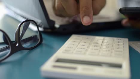 Hands-of-a-man-calculating-expenses-from-mobile-phone-data-on-working-desk.