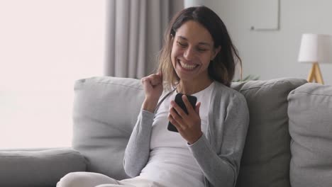 Feliz-chica-alegre-sosteniendo-teléfono-celebrar-la-victoria-móvil-en-casa