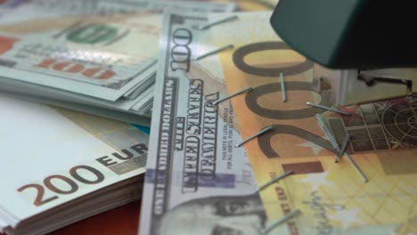 La-grapadora-sujeta-las-notas-de-dólar-y-euro-con-clips-de-hierro.-Grapadora-con-clips-de-papel-en-el-fondo-de-los-billetes.-Dinero-falsificado