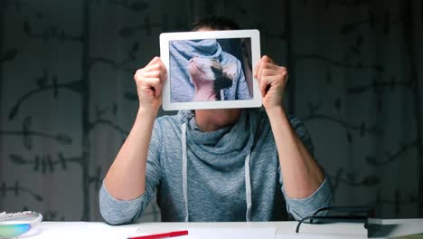 A-man-holds-a-tablet-in-his-hands-while-sitting-at-a-table.