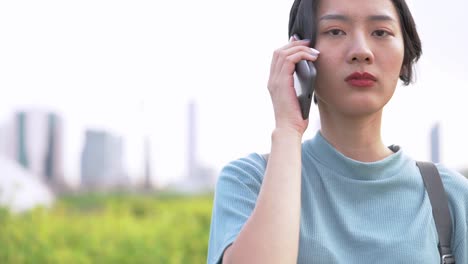 Cara-de-cerca-de-la-mujer-asiática-usando-el-teléfono-inteligente.-Cara-femenina-feliz-con-la-cara-bonita-posando-para-el-retrato-de-cerca-al-aire-libre.