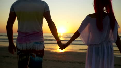 Romantic-couple-holding-hands-and-walking-on-the-beach-towards-the-sea