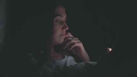 Young-woman-using-cellphone-on-bed-at-night