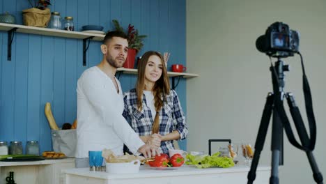 Cheerful-attractive-couple-recording-video-blog-about-vegetarian-healthy-food-on-dslr-camera-in-the-kitchen-at-home