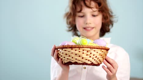 Portrait-of-a-cheerful-curly-red-haired-boy-with-an-Easter-basket-in-hands-on-a-blue-background