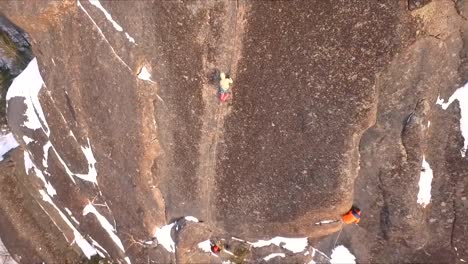 Aerial-view-of-a-rock-climber-climbing-a-steep-cliffs-during-a-sunny-winter-day.