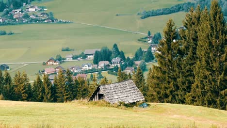 Acogedora-casa-de-madera-vintage-muy-antiguo-en-los-Alpes-austriacos-en-una-colina-con-pasto-verde-en-el-fondo-de-nuevas-casas-modernas,-casa-de-madera-viejo-país-rural-en-el-pueblo