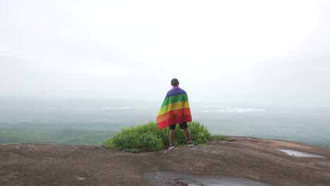 Mann-erhöhen-Regenbogen-Farbe-LGBTI-Fahnenschwingen-in-harten-Wind-auf-Mountain-Top-Sicht