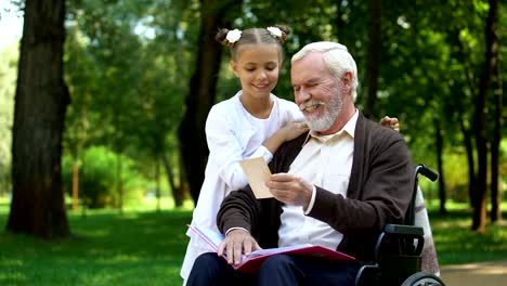 Handicapped-grandpa-showing-to-granddaughter-family-photos-telling-about-granny