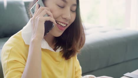 Beautiful-smart-business-Asian-woman-in-smart-casual-wear-working-on-laptop-and-talking-on-phone-while-sitting-on-table-in-creative-office.-Lifestyle-women-working-at-home-concept.