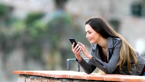 Excitada-mujer-comprobando-contenido-del-teléfono-en-un-balcón