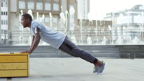 Afrikanischer-Mann-tun-Liegestütze-auf-Bank-in-der-Nähe-von-Brunnen