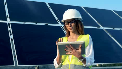 One-engineer-with-a-tablet-smiles-at-camera,-standing-near-sun-batteries,-close-up.