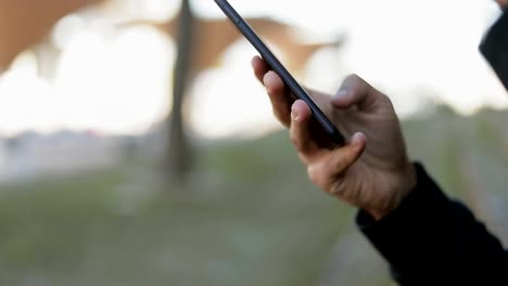 Closeup-of-young-mans-texting-on-phone,-holding-takeaway-coffee