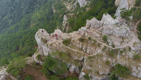 Aerial-top-view:-tourists-sit-on-top-of-mountain-cliff-on-summer-day