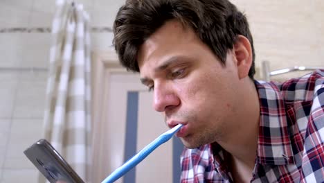 Young-man-cleans-his-teeth-and-looking-at-phone-in-the-bathroom.