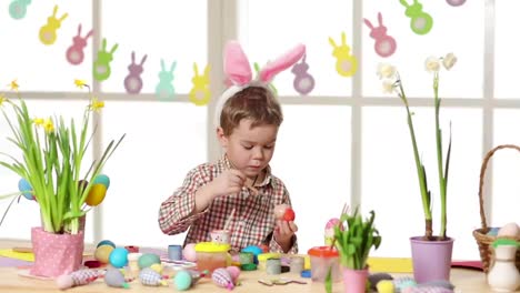 Niño-feliz-vistiendo-orejas-de-conejo-pintando-huevos-el-día-de-Pascua.